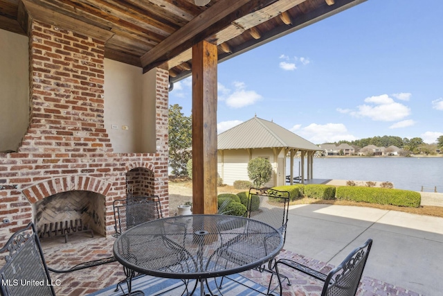 view of patio / terrace featuring outdoor dining space, a gazebo, an outdoor brick fireplace, and a water view