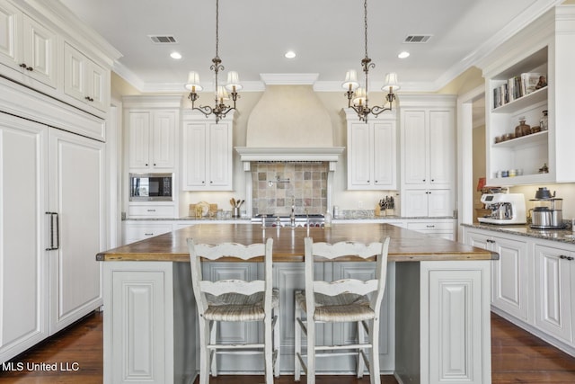 kitchen featuring built in microwave, visible vents, a notable chandelier, and custom range hood