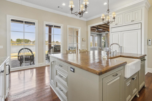 kitchen with a sink, dark wood finished floors, ornamental molding, hanging light fixtures, and a kitchen island with sink