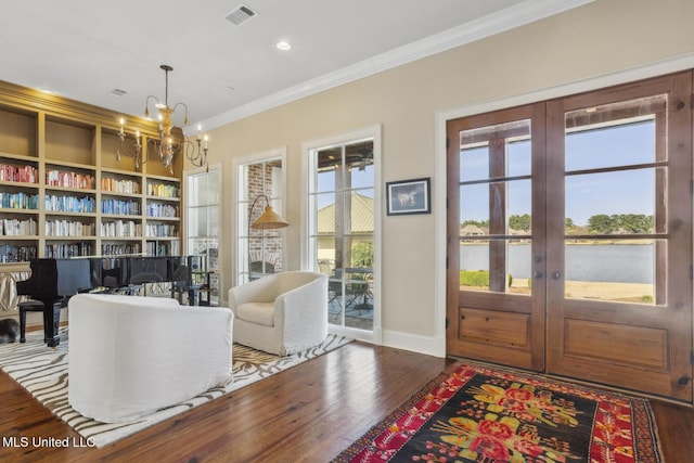 living area with wood finished floors, visible vents, french doors, crown molding, and a notable chandelier