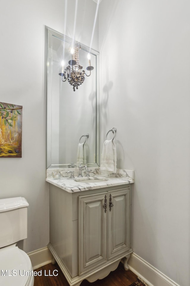 bathroom with vanity, toilet, wood finished floors, and baseboards