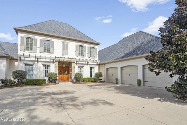 colonial house featuring stucco siding, an attached garage, concrete driveway, and roof with shingles