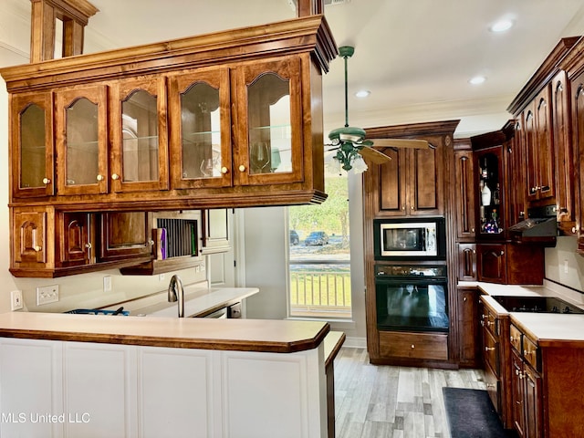 kitchen featuring black appliances, light wood-type flooring, ornamental molding, ornate columns, and kitchen peninsula