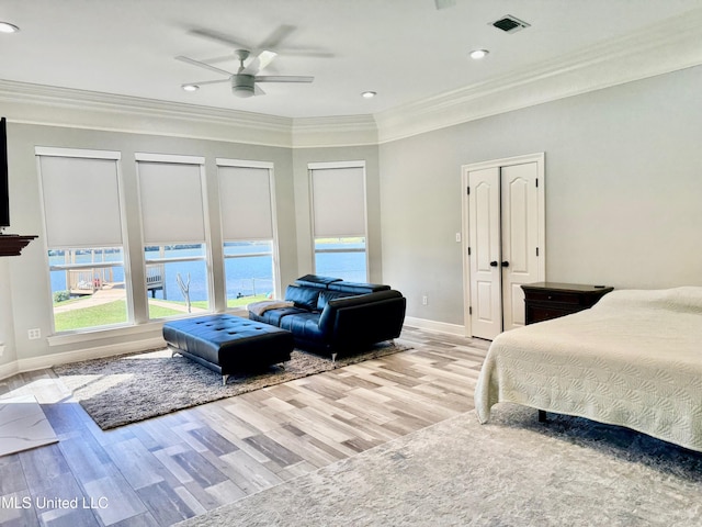 bedroom with a water view, crown molding, ceiling fan, light hardwood / wood-style floors, and multiple closets