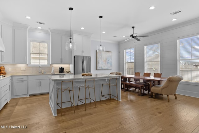 kitchen featuring a breakfast bar, stainless steel refrigerator, white cabinets, hanging light fixtures, and a center island