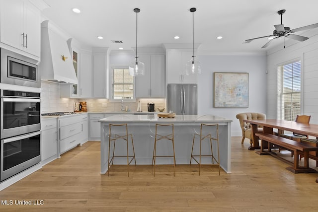 kitchen with a kitchen island, white cabinetry, custom exhaust hood, and appliances with stainless steel finishes