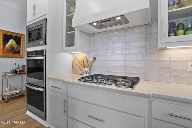 kitchen with white cabinetry, stainless steel appliances, light hardwood / wood-style floors, and custom exhaust hood