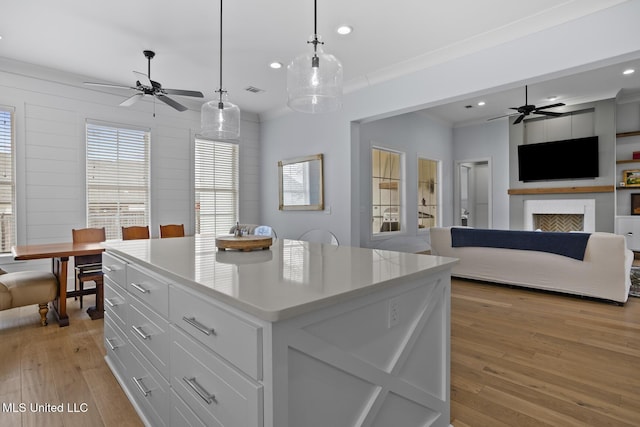 kitchen with white cabinetry, decorative light fixtures, light hardwood / wood-style floors, and a center island