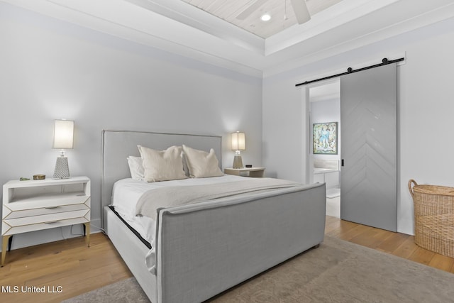 bedroom featuring hardwood / wood-style flooring, ensuite bath, a barn door, and a raised ceiling