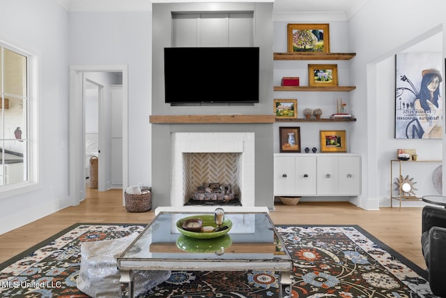 living room with ornamental molding, a brick fireplace, and light wood-type flooring