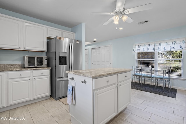 kitchen featuring light stone counters, a toaster, a kitchen island, visible vents, and stainless steel refrigerator with ice dispenser