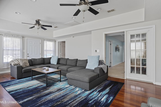 living area with a tray ceiling, visible vents, baseboards, and wood finished floors