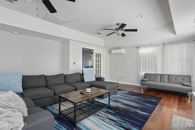 living room featuring wood-type flooring, a raised ceiling, visible vents, a wall mounted air conditioner, and baseboards