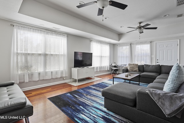 living area featuring a raised ceiling, visible vents, baseboards, and wood finished floors