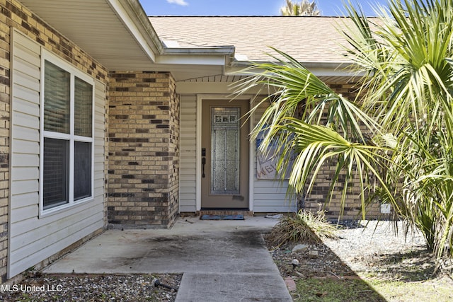 entrance to property with a shingled roof and brick siding