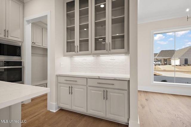 kitchen featuring white cabinets, glass insert cabinets, light stone counters, oven, and built in microwave