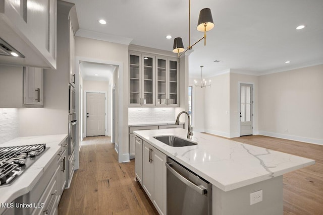 kitchen featuring a kitchen island with sink, decorative light fixtures, stainless steel appliances, a sink, and glass insert cabinets