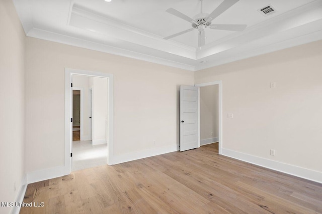 unfurnished room with light wood finished floors, visible vents, a tray ceiling, and crown molding