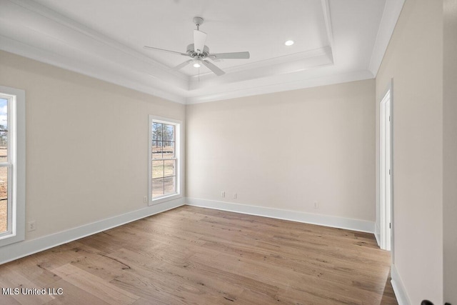 empty room with light wood-type flooring, baseboards, a tray ceiling, and crown molding