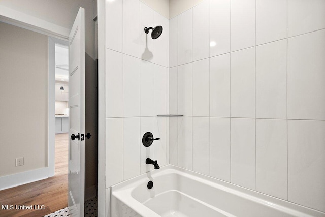 bathroom with baseboards, wood finished floors, and bathing tub / shower combination