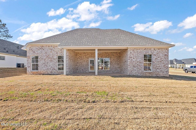 rear view of property with roof with shingles, a lawn, and brick siding