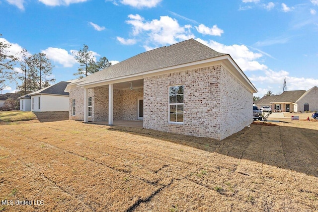 rear view of property with a shingled roof, a patio area, a lawn, and brick siding