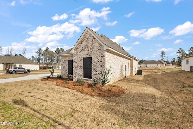 view of side of home with cooling unit, brick siding, a yard, and a residential view