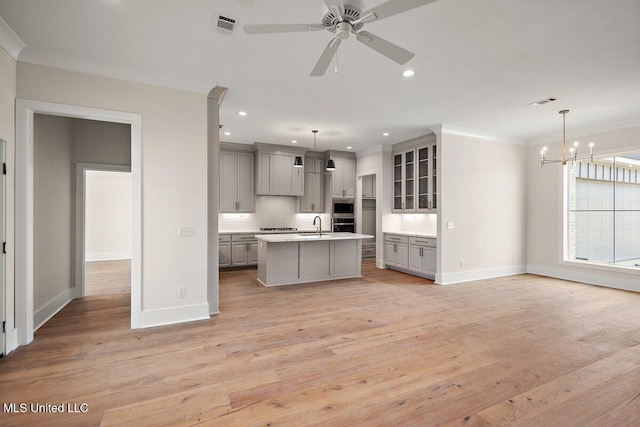 kitchen featuring pendant lighting, a center island with sink, gray cabinets, light countertops, and glass insert cabinets