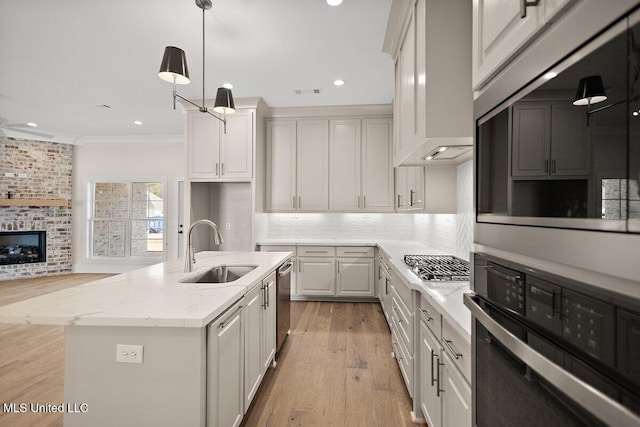 kitchen with a sink, white cabinets, appliances with stainless steel finishes, light stone countertops, and an island with sink