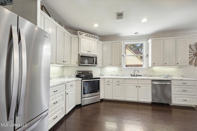 kitchen with light stone countertops, stainless steel appliances, dark wood-type flooring, sink, and white cabinets