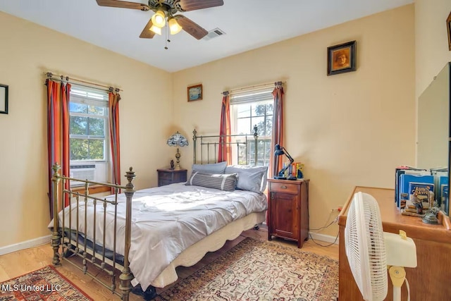 bedroom featuring visible vents, a ceiling fan, cooling unit, light wood-style floors, and baseboards