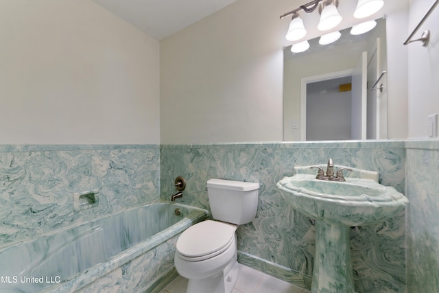bathroom with toilet, tile walls, tile patterned floors, a bath, and a wainscoted wall