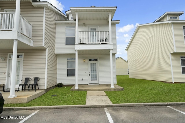 exterior space with covered porch, a balcony, a front yard, and uncovered parking