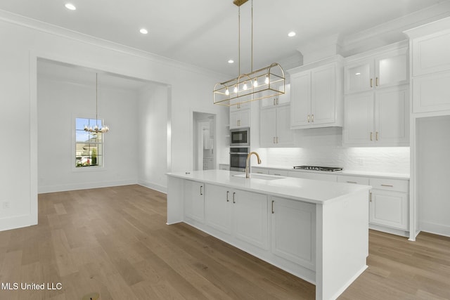 kitchen with white cabinets, appliances with stainless steel finishes, pendant lighting, and an island with sink