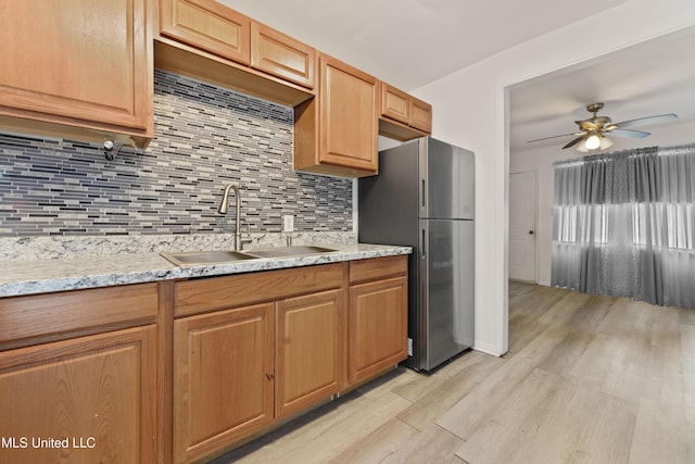 kitchen with freestanding refrigerator, ceiling fan, a sink, tasteful backsplash, and light wood-type flooring