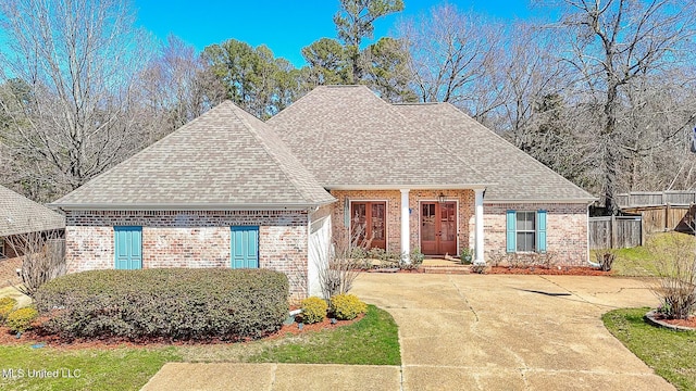 view of front of home with concrete driveway, fence, brick siding, and roof with shingles