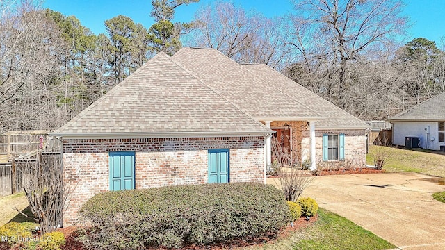 view of front facade with brick siding, central AC unit, and a shingled roof