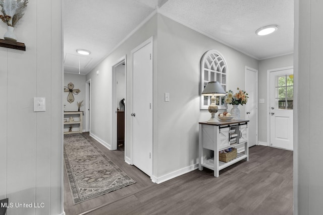 hallway featuring attic access, wood finished floors, baseboards, a textured ceiling, and crown molding
