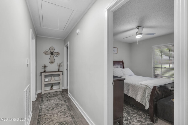 hall with attic access, wood finished floors, baseboards, and a textured ceiling