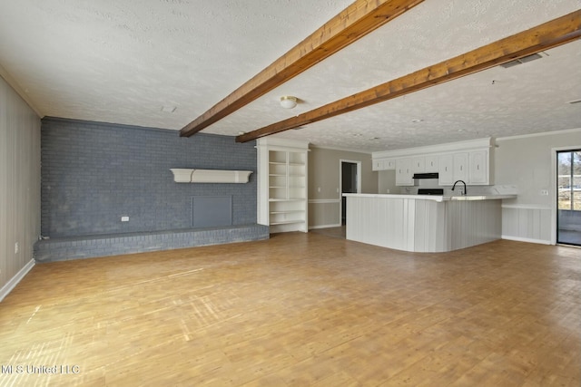 unfurnished living room featuring a brick fireplace, beam ceiling, light hardwood / wood-style flooring, and a textured ceiling