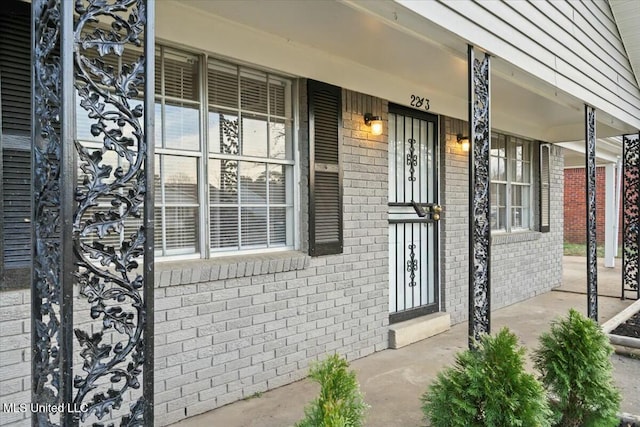 doorway to property with a porch and brick siding