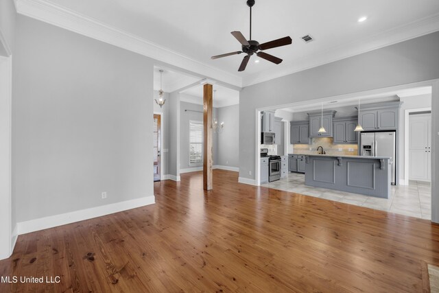 unfurnished living room with a ceiling fan, visible vents, ornamental molding, and a sink