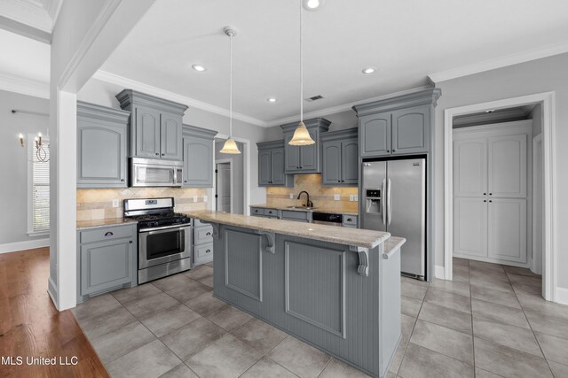 kitchen featuring a kitchen island, light stone counters, a sink, appliances with stainless steel finishes, and gray cabinetry