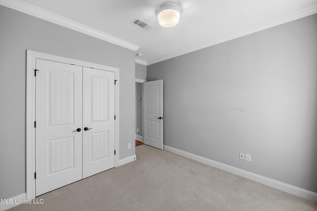 unfurnished bedroom with visible vents, baseboards, a closet, ornamental molding, and carpet