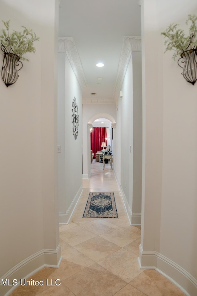 hallway with arched walkways, crown molding, and baseboards