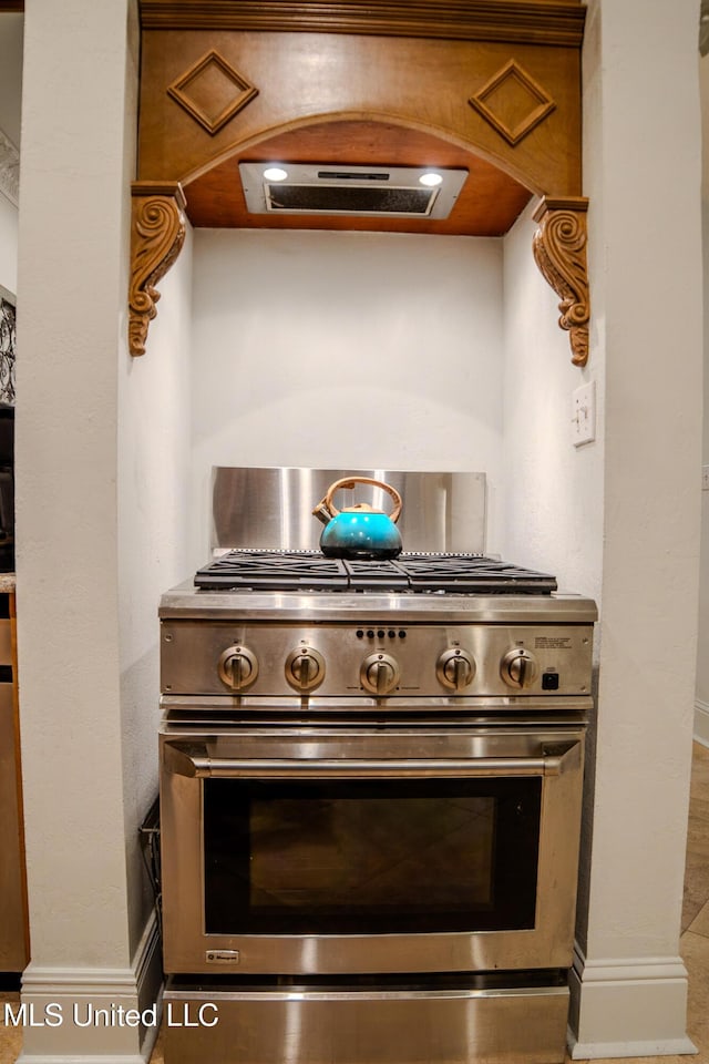 details featuring high end stainless steel range oven, exhaust hood, and baseboards