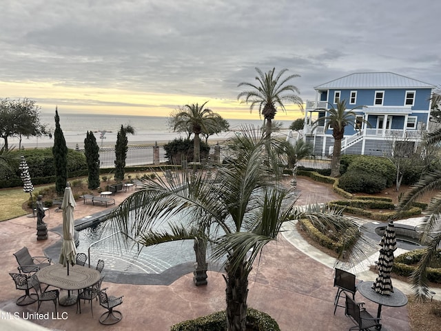 view of community featuring a pool, a water view, a patio area, fence, and stairs