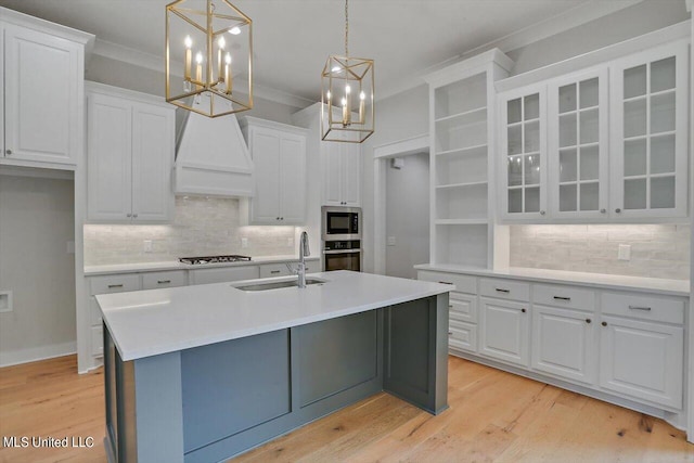 kitchen featuring hanging light fixtures, white cabinetry, custom range hood, sink, and stainless steel appliances