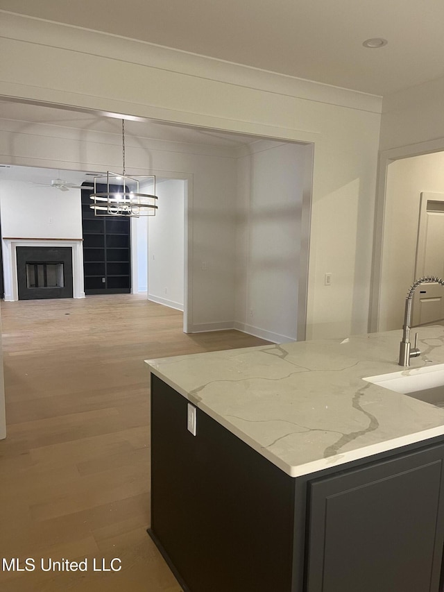 kitchen with light stone countertops, sink, a notable chandelier, pendant lighting, and wood-type flooring