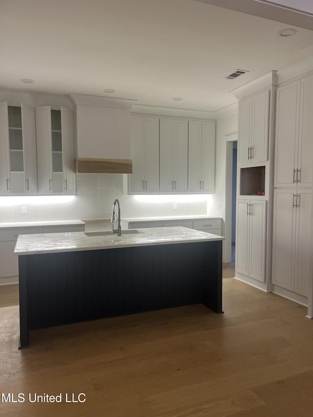 kitchen with sink, white cabinetry, an island with sink, and light hardwood / wood-style flooring